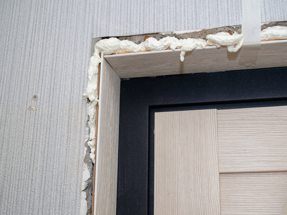 Close-up of a door frame with visible expanding foam insulation around the edges, partially finished wall and taped section above.