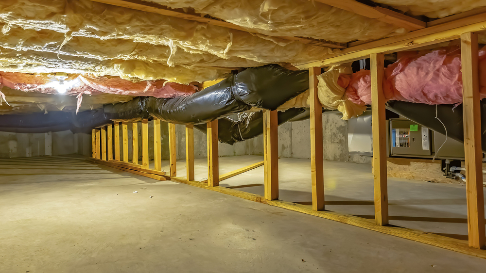 A basement or crawl space with exposed insulation, wooden framing, ductwork, concrete floor, and HVAC equipment in the background.